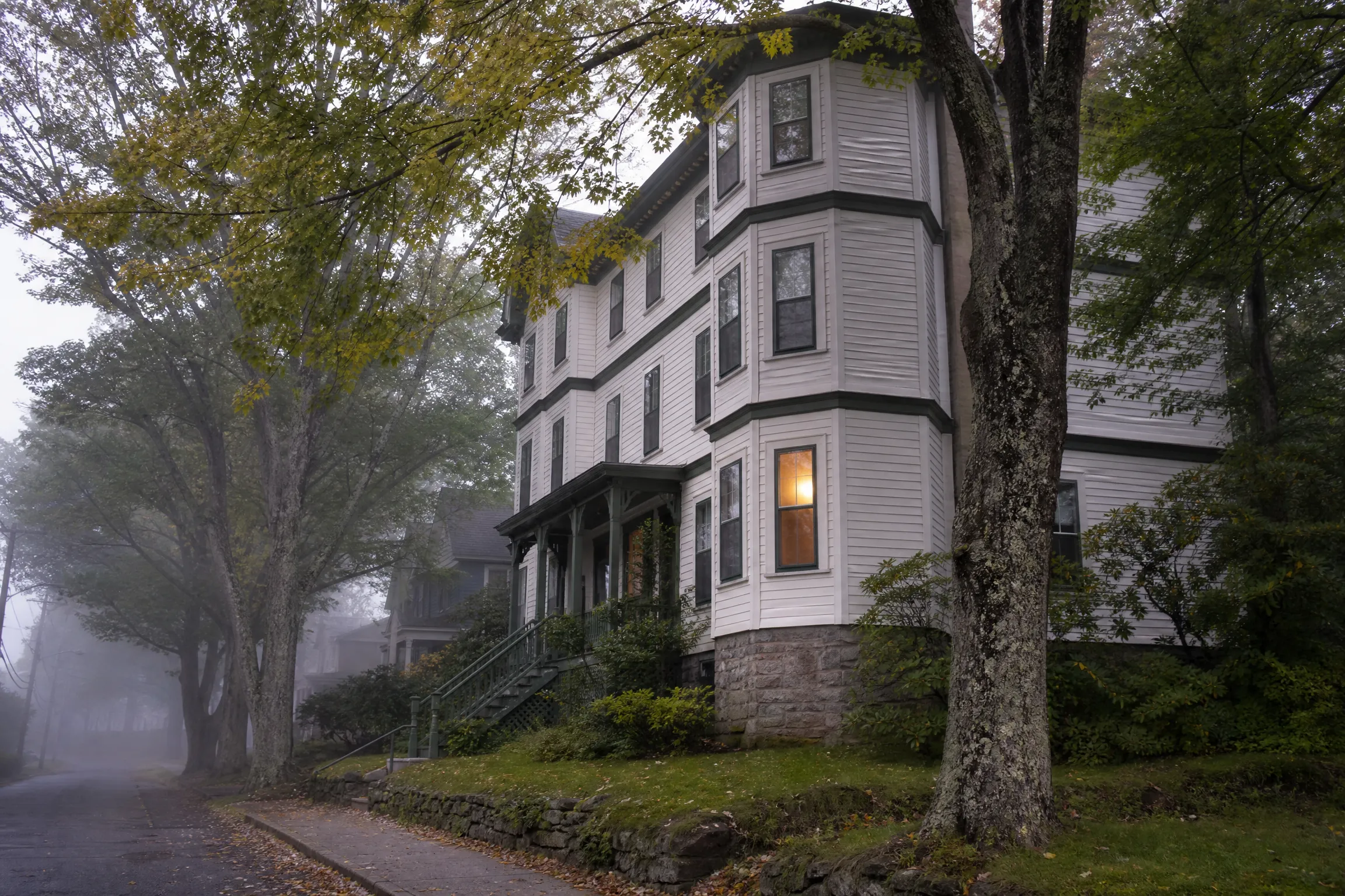White clapboard triple-decker home with a stone foundation on a foggy Portland, Maine street